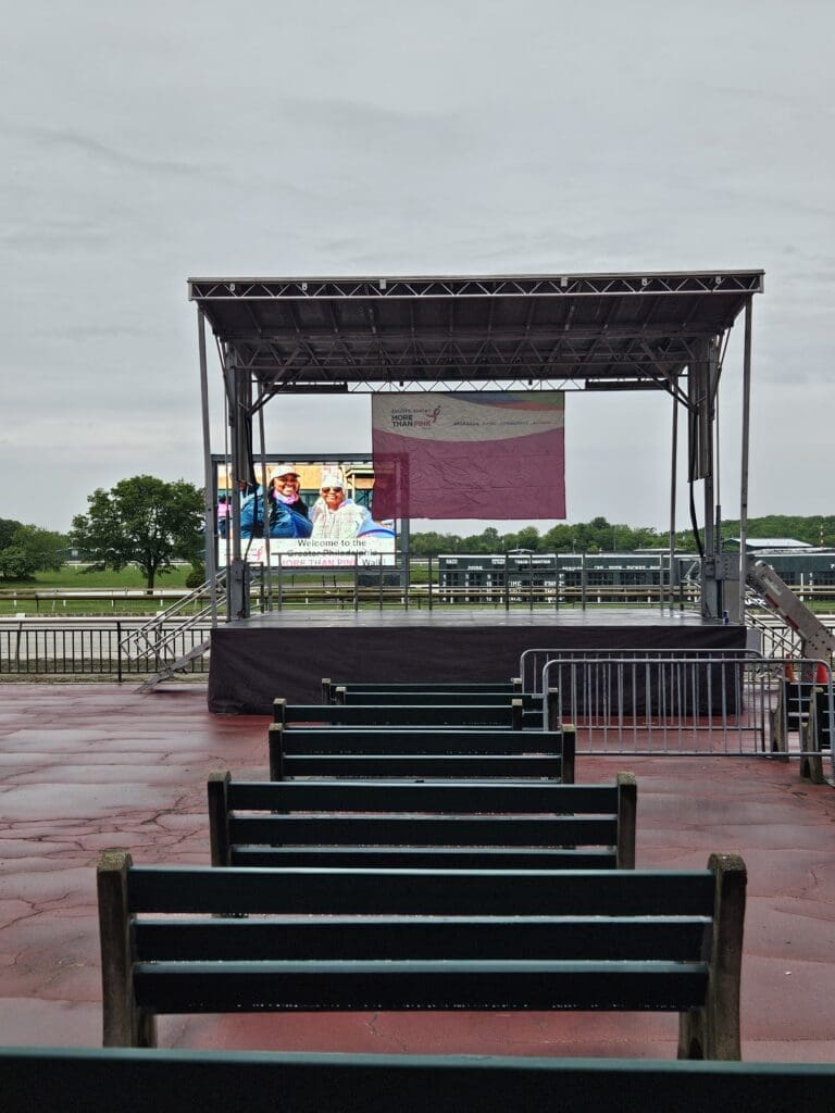 NYC portable event stage and bandshell rentals. A view of an outdoor event with chairs and tables. An event stage with an open top and a person walking on the grass to rent in Long Island and Tri state area from Allseasonsstagerentals.com