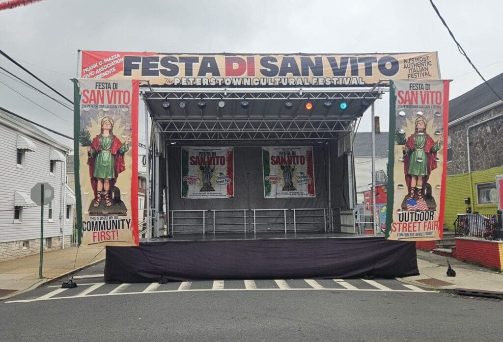 A stage with an image of the mexican flag on it. Festa di San Vito festival stage rental A view of an outdoor event with chairs and tables. An event stage with an open top and a person walking on the grass to rent in Long Island and Tri state area from Allseasonsstagerentals.com