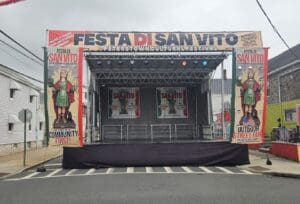 A stage with an image of the mexican flag on it. Festa di San Vito festival stage rental A view of an outdoor event with chairs and tables. An event stage with an open top and a person walking on the grass to rent in Long Island and Tri state area from Allseasonsstagerentals.com